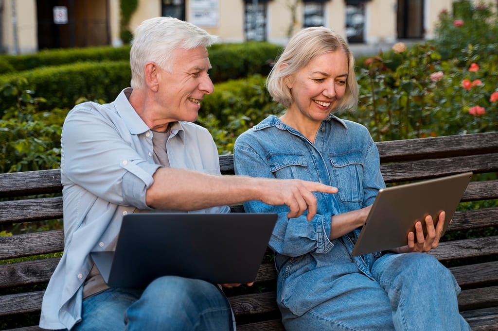 Happy senior couple on a bench outdoors looking at the laptop