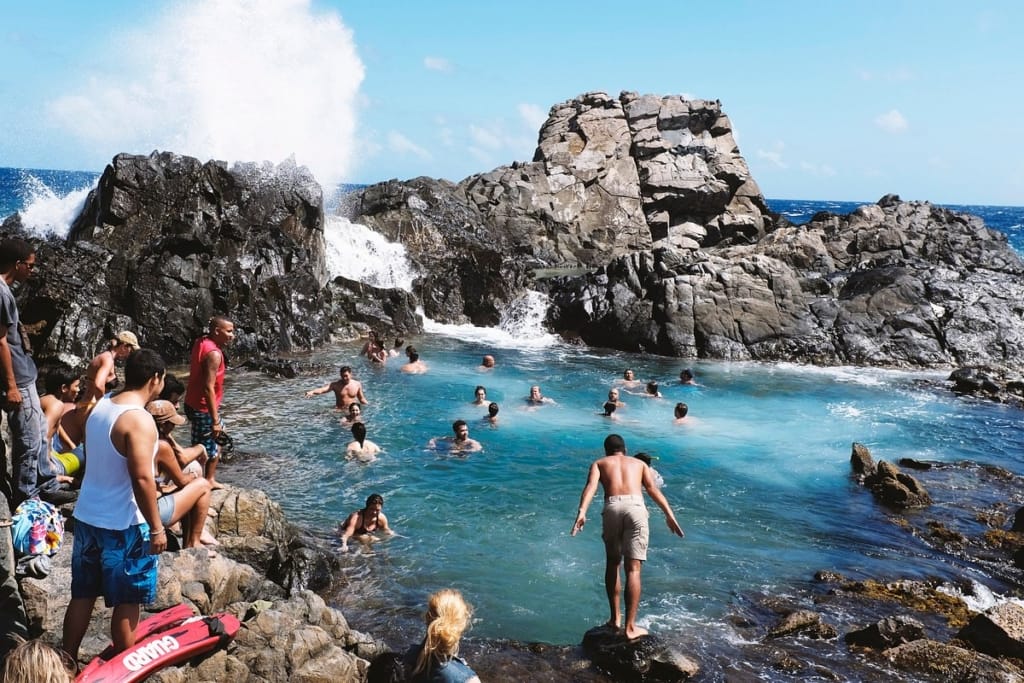 Swimmers in a natural rock pool in Aruba, one of the warm getaways outside the U.S.
